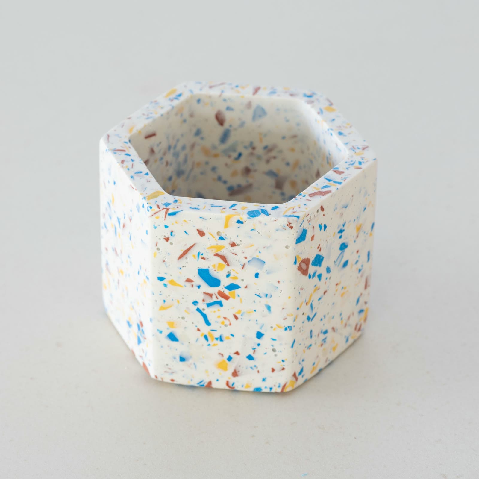 Zeshoekig wit terrazzo bloempotje met blauwe, gele en roodbruine spikkels