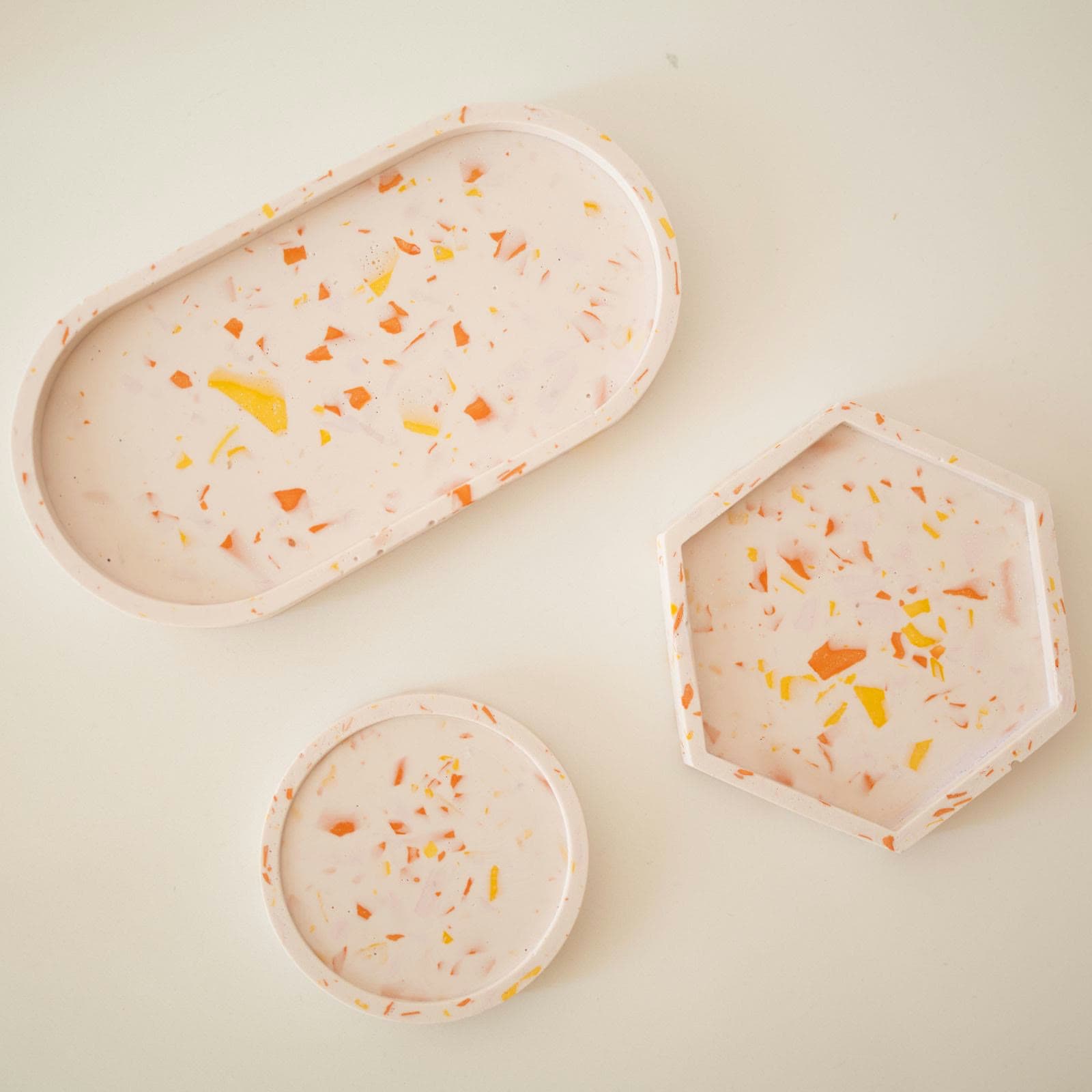 Drie witte terrazzo schaaltjes naast elkaar, ovaal, zeshoekig en rond, met oranje en gele spikkels