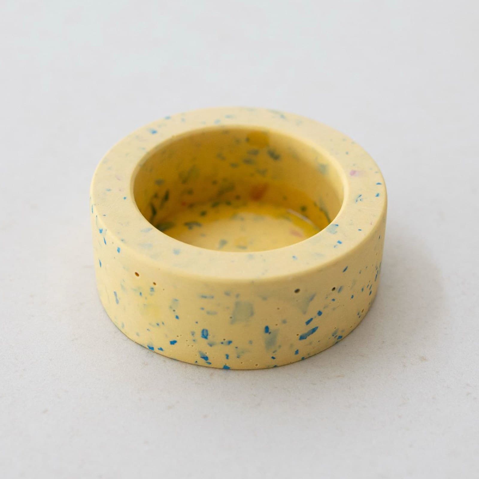 Ronde zachtgele terrazzo theelichthouder met blauwe spikkels, van schuin boven