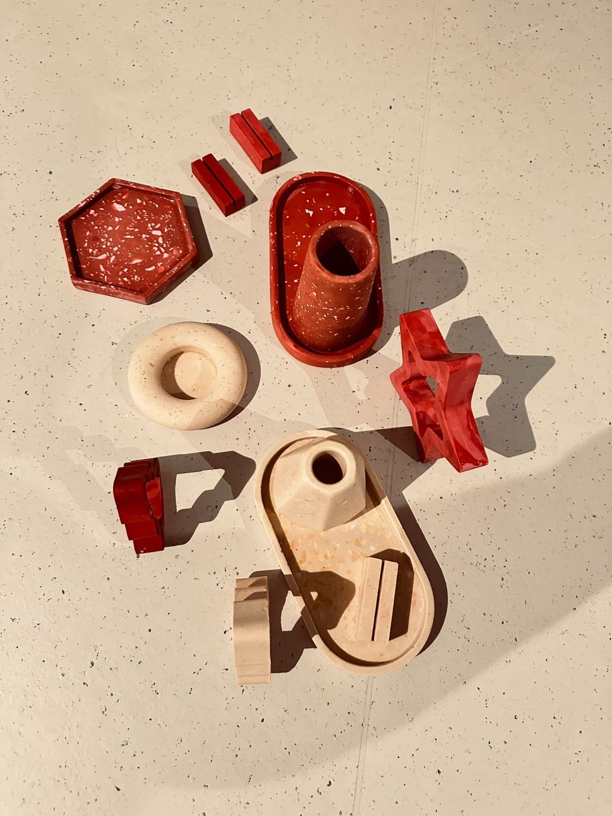 Zelfgemaakte terrazzo stukken in rood en crème: een zeshoekig schaaltje, een vaasje op een ovale tray, een ster en kaarthouders